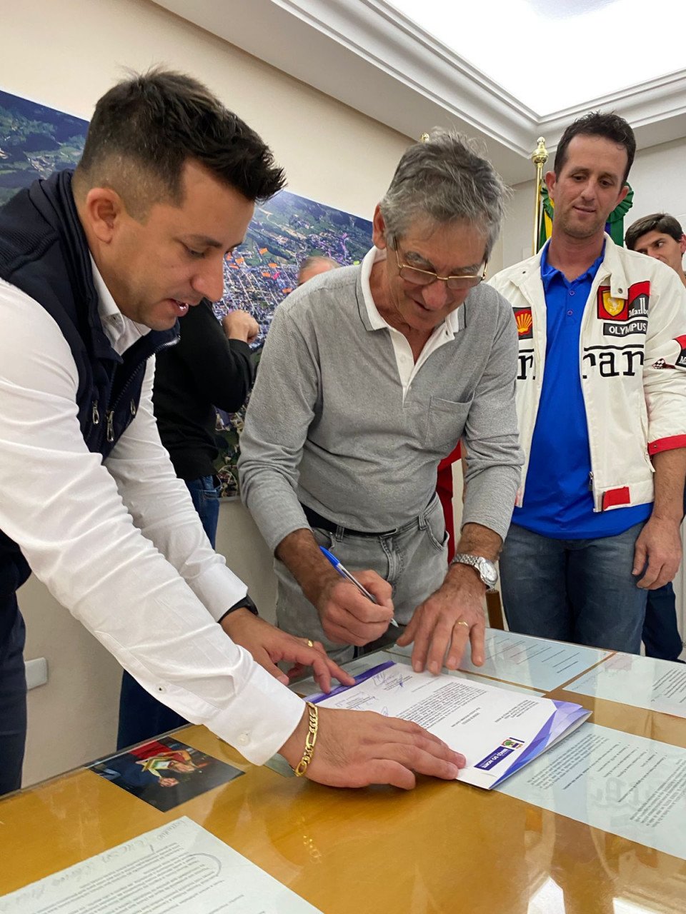 Azeiteiro #ParaTodosVerem Na foto, o prefeito de Braço do Norte, Beto Kuerten Marcelino, e um representante da empresa Dutra Pré-Moldados assinam a ordem de serviço para a pavimentação da Estrada do Azeiteiro