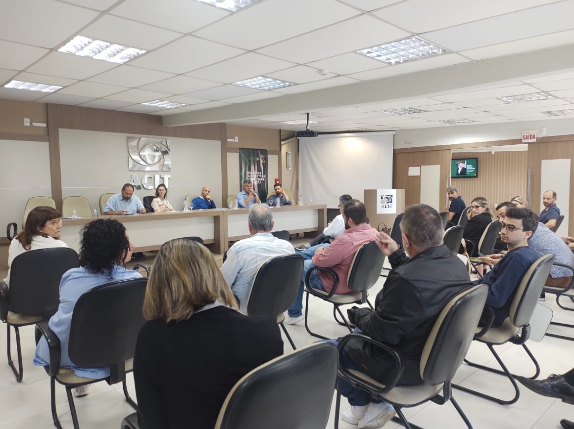 entidades #Pracegover Foto: na imagem há pessoas, mesa, cadeiras e um quadro