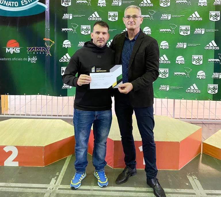 Jaison Judô #ParaTodosVerem Na foto, um homem alto e grisalho entrega uma certificação de graduação para um outro homem, mais baixo e moreno