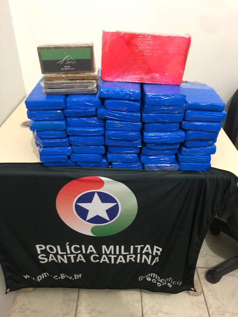 Droga Imbituba #ParaTodosVerem Na foto, em cima de uma mesa há diversos blocos de drogas