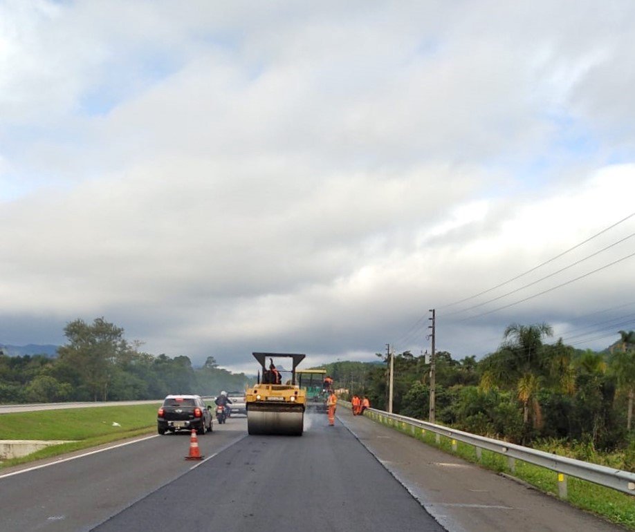 Cronograma de Obras - CCR ViaCosteira BR101 #ParaTodosVerem Na foto, um rolo compressor é operado em uma rua lateral à BR-101