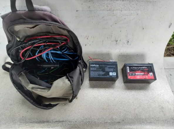 Furto Imbituba #ParaTodosVerem Na foto, em cima de um banco há uma mochila preta com vários fios elétricos e, ao lado, duas baterias