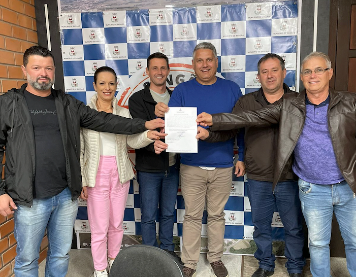 Sangão #ParaTodosVerem Na foto, um grupo de pessoas comemoram a entrega da ordem de serviço para a pavimentação asfáltica de dois trechos da Rodovia dos Imigrantes, em Sangão