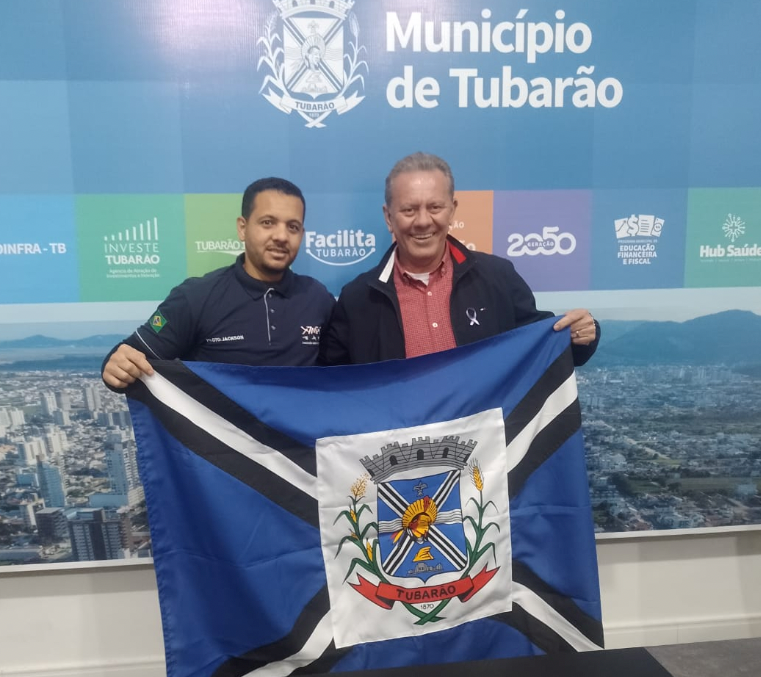 Aeromodelismo #ParaTodosVerem Na foto, dois homens seguram a bandeira do município de Tubarão