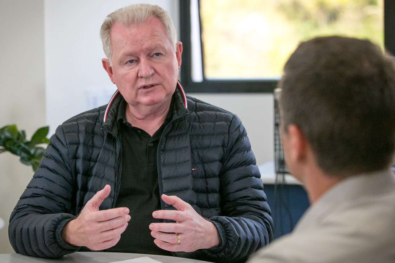 fotonoticia_010822_Entrevista_Stupp_RZE2 #ParaTodosVerem Na foto, um homem loiro vestindo uma jaqueta preta conversa com outro homem, que aparece de costas na imagem
