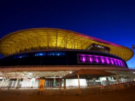 Vista noturna da Arena do Grêmio iluminada em tons de roxo e amarelo
